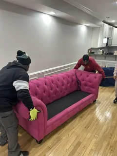 Three crew members lifting a pink tufted sofa