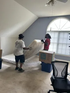 Two crew members carrying a mattress out of a bedroom