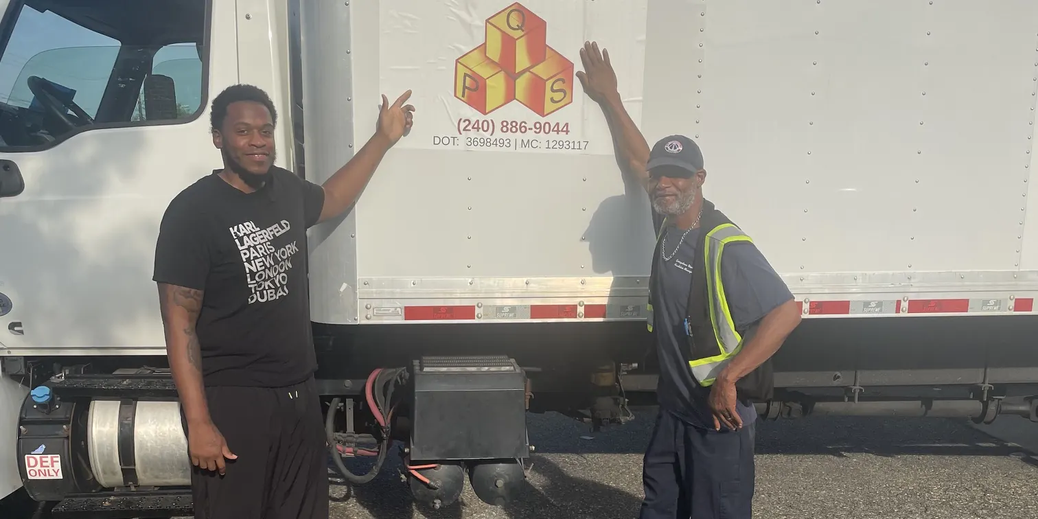 Two Quest crew members pointing to the company logo on a box truck